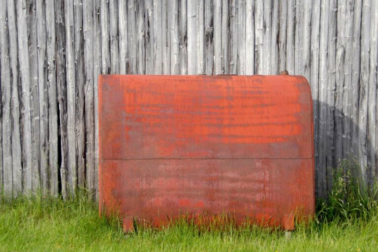 Citerne à mazout rouge devant une palissade en bois et posée sur l'herbe